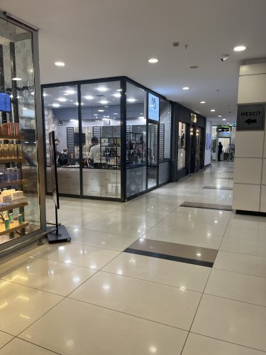 Entrance to Mert Okyay Men's Hair Salon inside Özdilek Mall in Eskişehir, with a customer receiving a haircut and a sign pointing toward the Mescit (prayer room).