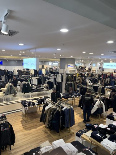 Shoppers browsing the men's clothing section at Özdilek Shopping Mall in Eskişehir, featuring international fashion brands like Tommy Hilfiger, Calvin Klein Jeans, and Guess.