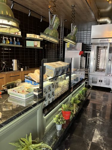 nterior view of the service counter at Nil Fırın in Eskişehir, featuring industrial-style green pendant lights, black subway tiles, decorative plants, and a professional Greenoks baking oven in the background.