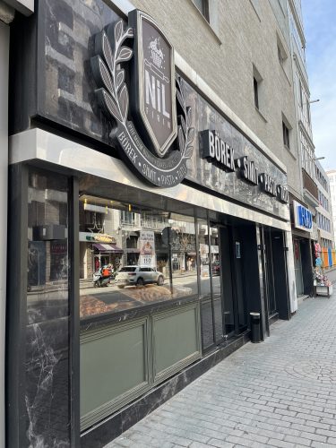 Exterior storefront of Nil Fırın (Bakery) in Eskişehir, featuring a black marble facade with signs for traditional Turkish Simit, Börek, and desserts, and fresh pastries visible in the window.